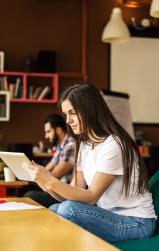 Brunette girl working with tablet computer sitting in coworking cafe office