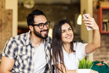 Two hipster students, bearded man and brunette girl taking selfie with smartphone in modern coworking office