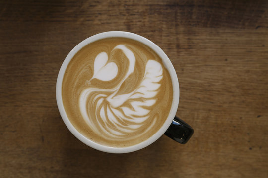 Overhead shot of coffee cup with elegant swan and heart latte art on a warm wooden background