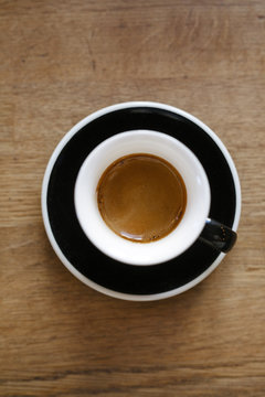 Overhead shot of a hot espresso in a minimalist white cup on a wooden table