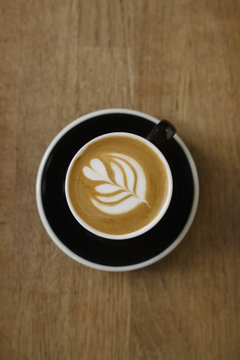 Top Down View of Latte Art Coffee in Black Cup on Rustic Wooden Table