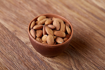 Ceramic bowl of almonds on wooden background, top view, close-up, selective focus.
