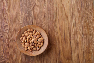 Ceramic bowl of almonds on wooden background, top view, close-up, selective focus.