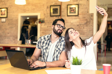 Freelance workers, bearded man and brunette girl taking selfie with smartphone in modern coworking office