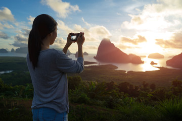 Woman take a photo, sea and mountain with sunrise background.