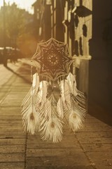 Handmade mandala God's Eye dream catcher with white peacock feathers and amethyst crystals on city background in Krakow