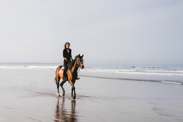 woman riding horse on sandy beach with ocean behind