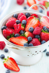 Fresh berries - strawberries, raspberries and blueberries - in a while colander on white wooden background