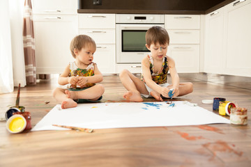 Fototapeta premium Two brothers paint with paint on a large white sheet of paper.