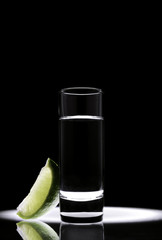 a glass of tequila with a piece of lime on a black background