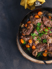 Stewed pork cheeks with vegetables in an iron pan, with a dark background on an overhead shot. Spanish food. Copy space.