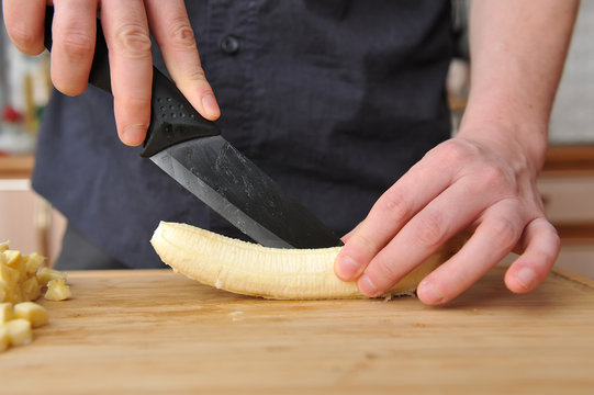 Man slices a banana with a large knife on a wooden board