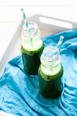 Healthy green smoothie made from spinach, apple and cucumber in a jars with red straw on white wooden table