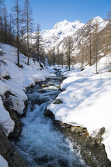 Alpine valley with snow in spring, creek swollen by thaw