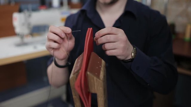 Man creates a brown leather wallet with his own hands with a needle in the leather workshop