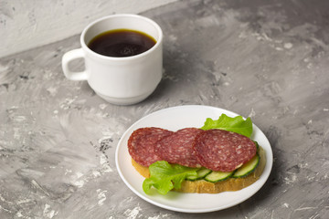 cup of black coffee and sandwich with sausage, cucumber and salad