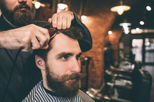 Close up of a bearded guy. His hairdresser is cutting and modelling his hair.