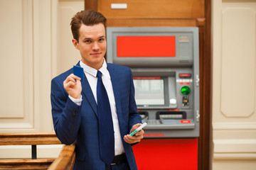 A young businessman stands near an ATM in a shopping center