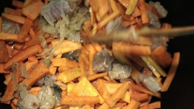 Preparation of rice dishes - pilaf from Uzbekistan. In a large saucepan roasts meat, garlic, carrots and spices.