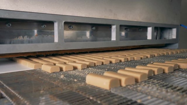 Snack bars go on a conveyor, while a factory machine cuts them. 4K.