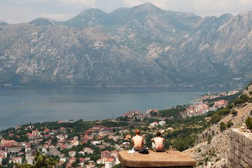 men traveles sitting on the top roof  and observing Kotor old city, gulf,  mountains in the sunny summer day
