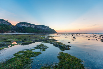Green rocks beach at Bali, Indonesia.Sunrise at Bali Beach with green seaweeds rocks by the beach.