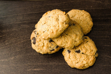 Group of delicious homemade oatmeal cookies with chocolate drops. Chaotic batch of tasty brown oatcakes on dark wooden table