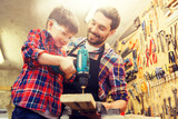 family, carpentry, woodwork and people concept - father and little son with drill perforating wood plank at workshop