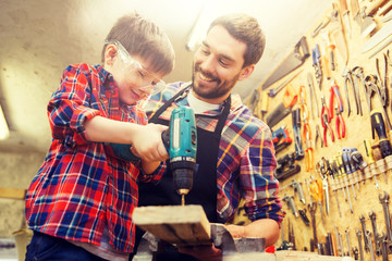 family, carpentry, woodwork and people concept - father and little son with drill perforating wood...