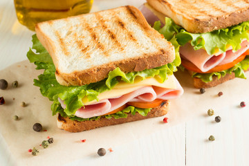 Close-up photo of a club sandwich. Sandwich with meet, prosciutto, salami, salad, vegetables, lettuce, tomato, onion and mustard on a fresh sliced rye bread on wooden background. Olives background.