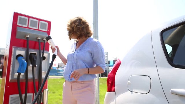 A woman at the charging station for electric vehicles pulls out the plug from car the socket 