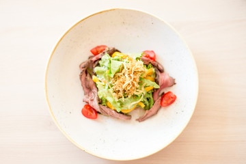 Vegetable salad with roast beef in white plate on table.Top view