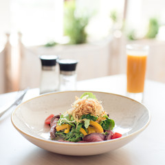 Vegetable salad with roast beef in white plate on table. Breakfast in  restaurant.