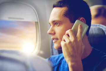 travel, tourism and technology concept - close up of young man calling on smartphone in plane and looking into porthole