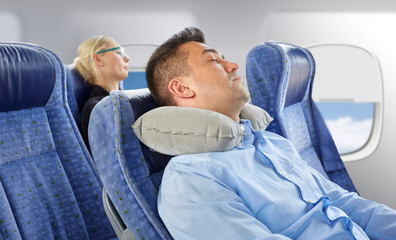 travel, comfort and people concept - man sleeping in plane with inflatable cervical neck pillow over porthole background