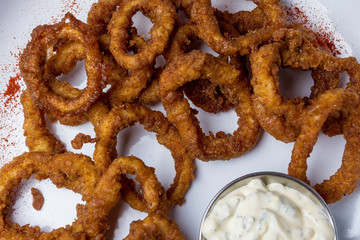 Close-up of onion rings in batter with sauce. On a white plate. View from above. Close-up