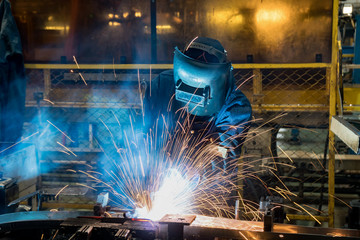 Industrial worker is welding in automotive part factory
