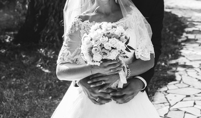 Wedding couple is hugging outdoors in the green park. Groom is embracing bride in white puffy...