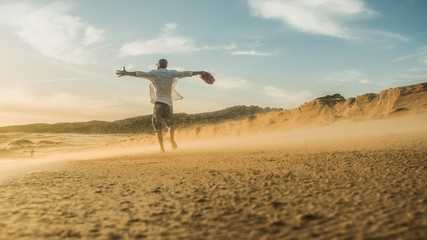 hipster MAN with tattoos and beard standing on a lonely windy beach with arms wide open enjoying...