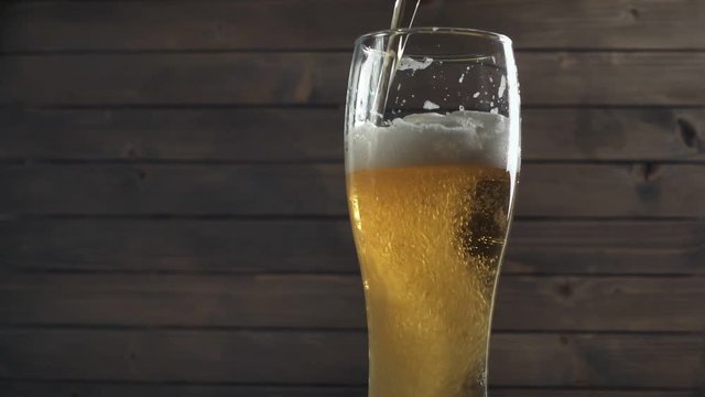 Beer poured in glass on wood background. Foam sliding down side. Slow motion