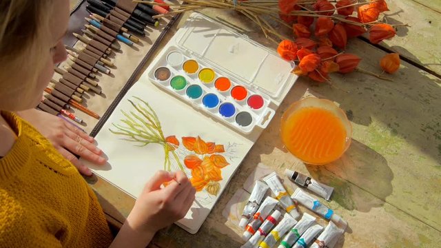 young female artist painting a picture of a red physalis plant in front of her