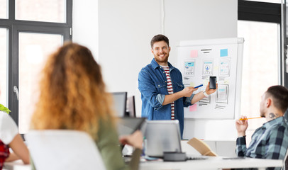 business, technology and people concept - man showing smartphone user interface design to creative team at office presentation