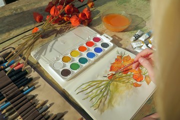 young female artist painting a picture of a red physalis plant in front of her