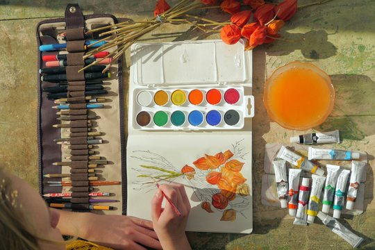young female artist painting a picture of a red physalis plant in front of her