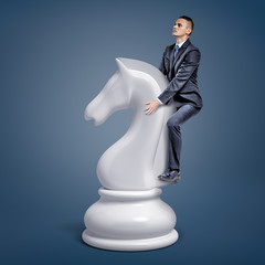 A tiny businessman rides a large white chess knight piece on a blue background. © gearstd