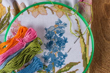 The process of cross-stitch. Canvas on hoops, needles, embroidery floss and pattern.