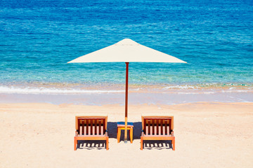 Summer holidays background wallpaper: two beach lounge chairs under tent on the beach.