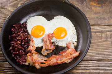 Bacon,Egg and bean. Salted egg and sprinkled with black pepper. English breakfast. Grilled bacon, two eggs and beans in pan on wooden table