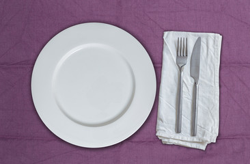Leerer Teller und Besteck auf violettem Stoff