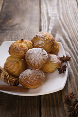 Delicious eclairs sprinkled with icing sugar, stand on a wooden table. Copy spase.